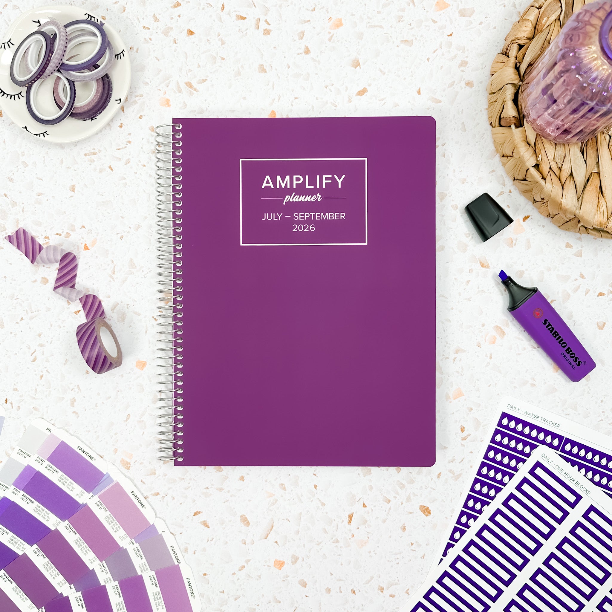 Daily Planner - July-September 2026 - Amplify Planner displayed on a desk with creative tools, showcasing its stylish purple cover.