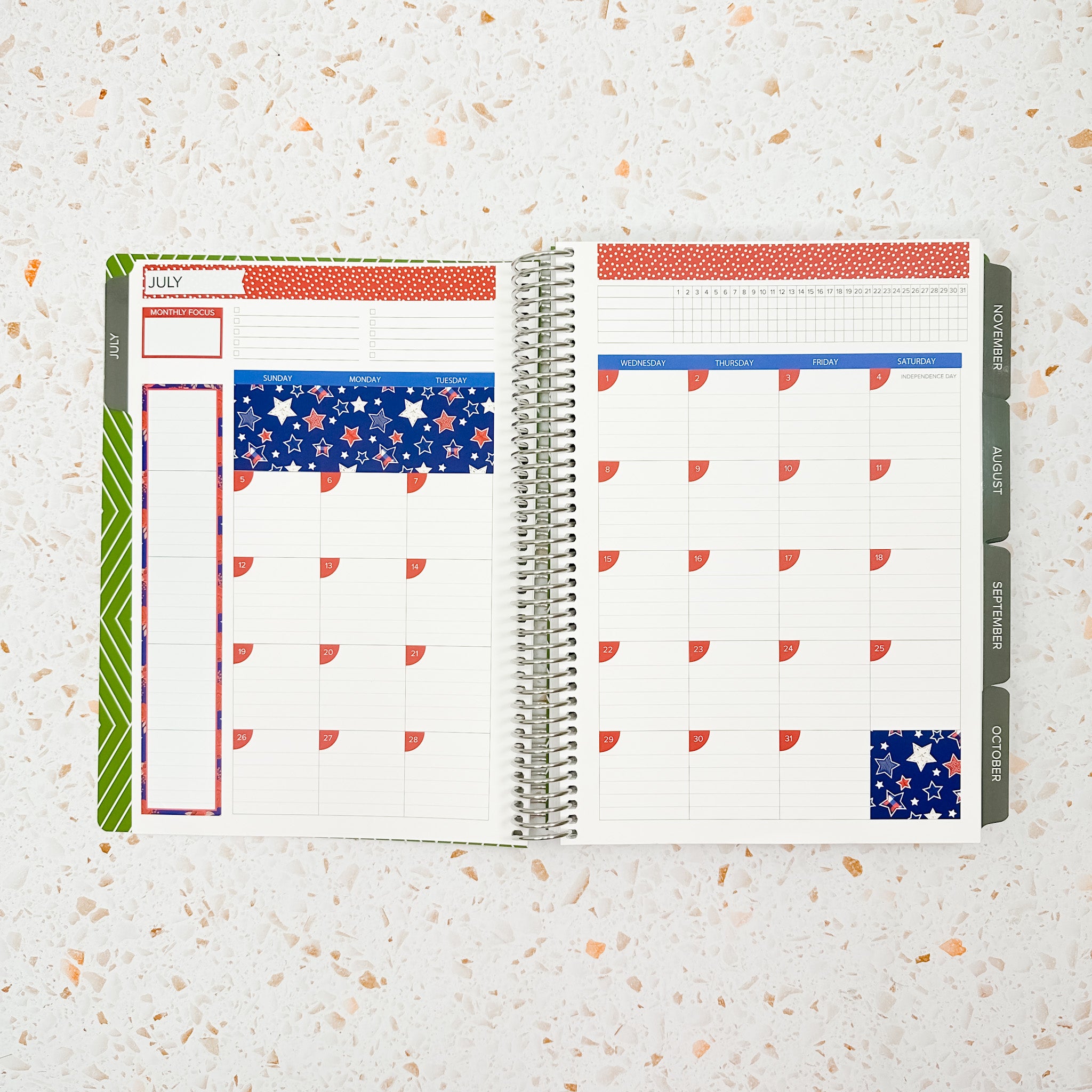 Open monthly planner spread decorated with the Stars & Stripes Monthly Sticker Kit featuring patriotic red, white, and blue star-patterned stickers, bold blue headers, and festive Fourth of July-inspired accents.