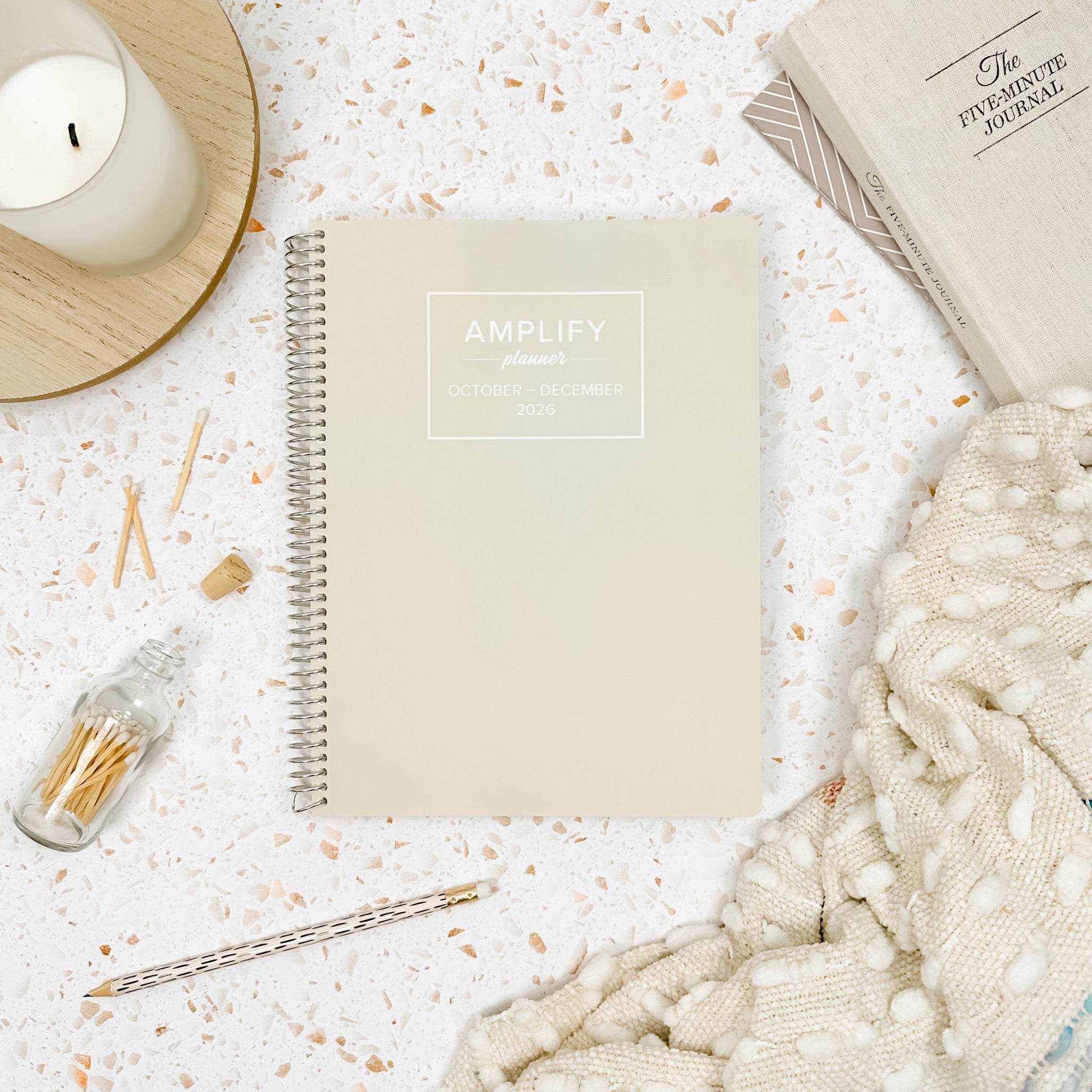 Daily Planner - October-December 2026 - Amplify Planner displayed on a desk with creative tools, showcasing its stylish tan cover.
