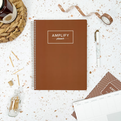 Begin Again Brown cover of undated daily Amplify Planner daily planner on a styled background with decorations