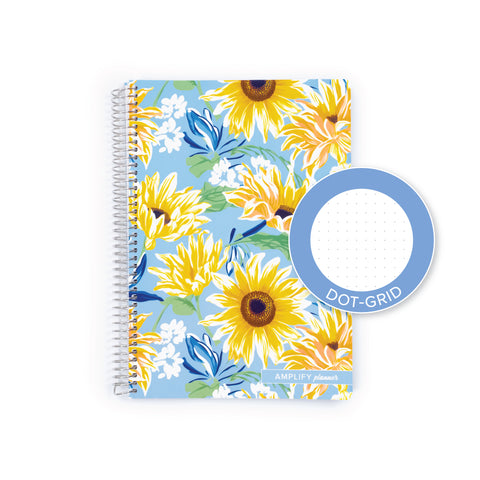A spiral-bound planner or notebook with a light blue cover decorated with a yellow sunflower and white floral pattern, shown on a white background with a blue circular inset labeled DOT-GRID.