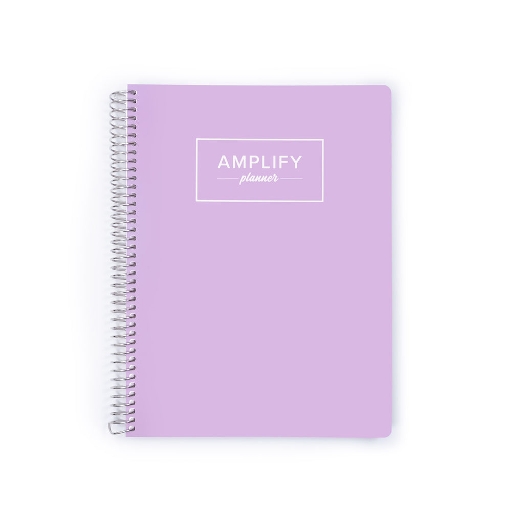 A lavender purple spiral-bound planner with a white logo reading 'AMPLIFY planner' on the front cover, shown on a plain white background.