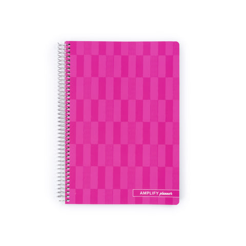 A pink spiral-bound planner with a checkerboard pattern on the cover, featuring the text 'AMPLIFY planner' in the bottom right corner, set against a plain white background.
